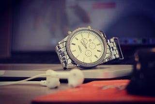 A silver mechanic watch on a laptop keyboard. Next to the laptop, there were a pair of wired Apple earbuds.