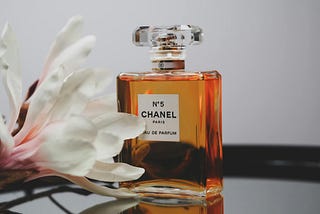 A bottle of Chanel №5 perfume sits on a table with a large white flower, elegantly framed against a minimalist background.