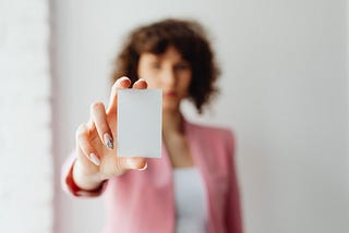 A young lady, blurred into the background, holds out a business card.