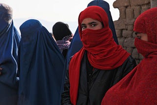 An Afghan girl looking directly at the camera amid women who are wearing burqa
