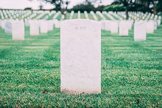 A graveyard of identical, plain tombstones in a grassy field. One tombstone is in focus.