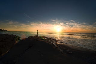 Person standing on mountain facing sun at golden hour