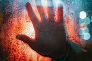 A hand pressed against a window with a red light background.