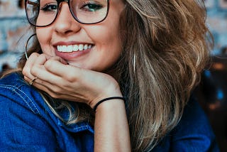 Young girl in a blue shirt, wearing glasses, smiling