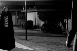 A female vampire wearing a chador stands looking at an unseen character.