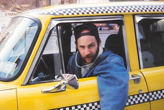 Bearded cab driver with baseball hat on backwards leaning out the window of an old time Checker taxicab