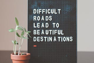 A quote: “difficult roads lead to beautiful destinations” on a peg board next to a potted plant