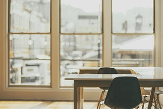 Office space with two white tables and two empty chaires near glass window