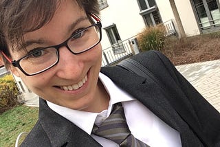 A selfie of a young nonbinary person wearing a suit and tie, smiling.