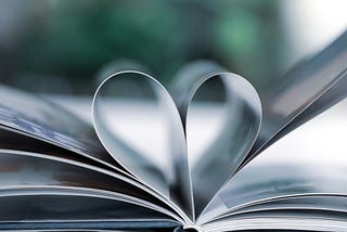 Black and white phote (just a tinge of green in the background) of an open book with the middle pages folded into the shape of a heart.