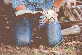 Man kneeling on the ground, holding an open Bible
