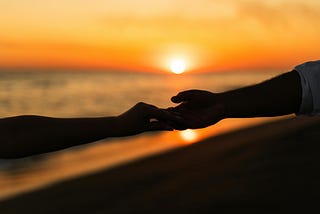 Silhouetted couple holding hands at sunset on the beach, symbolizing emotional connection and later-in-life love.