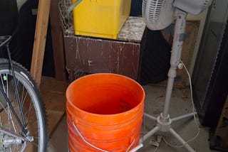 orange buckets, fan, window wash kit on a table in storage shed.