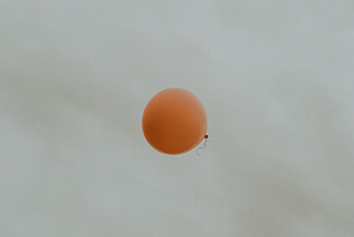 Orange balloon flying free in a grey sky.