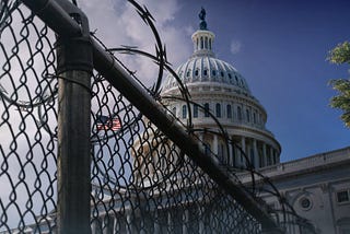The dome of the U.S. Capitol Building behind a chain-link fence with razor wire. Photo by John Webb/Getty Images