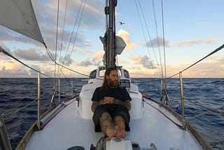 The author is lying on the deck of his sailboat at sea.