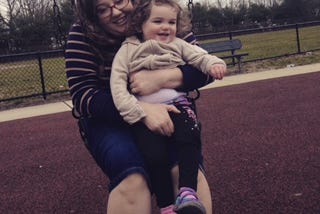 A mom and a little girl on a swing; wood chips on the ground