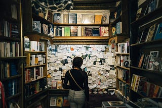 A woman looking at a bulletin board with many notes pinned to it.