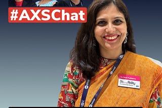 A woman named Shruti Pushkarna is smiling and wearing a colorful sari. She is wearing a name badge that reads “Disability” with a title under it. In the background, there are three individuals with a banner that says “#AXSChat.” The individuals are a man wearing sunglasses, a woman with purple hair, and another man wearing glasses.