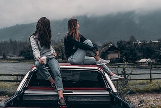 Two people sitting on roof of car looking away from each other