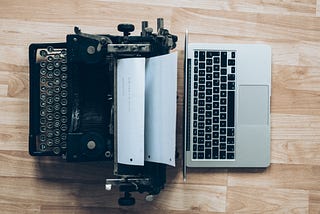 Black type writer and silver mac book resting on a wooden table.