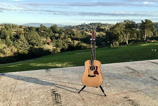 acoustic guitar sitting on the subfloor of a house about to be built, with expansive view of mountains in background