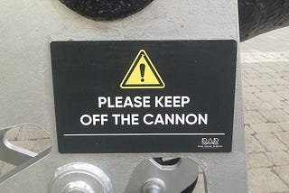 Close up of a warning sign that reads ‘Please keep off the cannon’ with a small logo reading ‘Royal Arsenal Riverside’. Taken in Woolwich, part of the Royal Borough of Greenwich.
