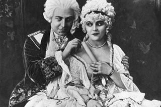 A still image from a black and white film. A male aristocrat is seducing a coquettish young woman… or vice versa.