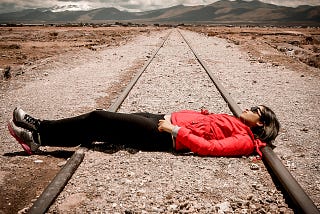 A woman in what appears to be a desert lying on railroad tracks.