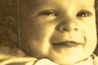 A baby with soft eyes, wearing white. A quiet, tender moment captured.