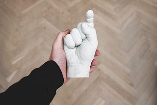 A hand holding a white statue with the shape of a hand pointing towards the reader