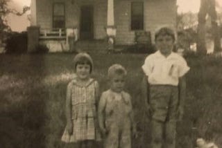 Black and white photo of three children posed in front of a house