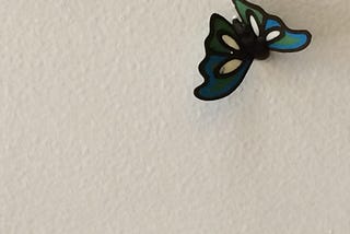 A blue green ceramic butterfly sits on the white washed wall.