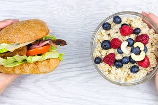 Image of one hand holding a burger and the other hand holding oatmeal with berries