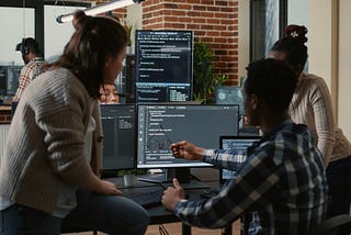 Three individuals looking at some code on a computer screen.