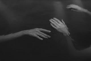 Image shows Grayscale Photo of Hands Floating on Water