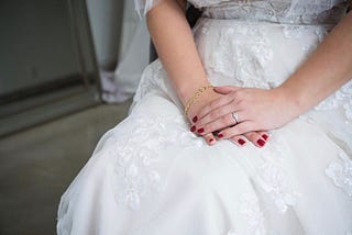 A bride’s hands are folded in her lap, engagement ring adorning her rouge painted fingers. Feels hopeful, expectant.