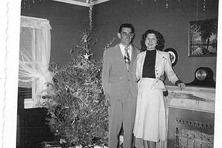A black and white photo of a man and woman on their wedding day in 1953. There’s a Christmas tree in the background.