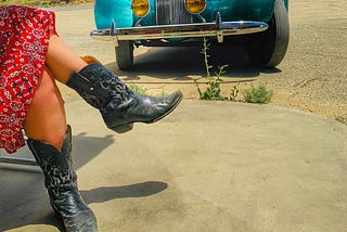 A woman’s legs with cowboy boots and the bottom of a red dress