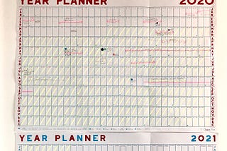 An image of a 2020 wall calendar with various trips and treats scribbled out and a yellow line through each day of quarantine