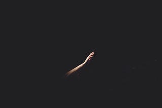 A hand reaches through the darkness