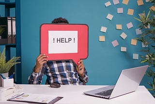 Employee holding a speech bubble with the word help while working at a computer