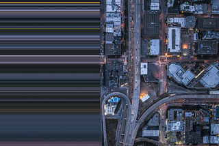 Aerial view of a city in the evening. The right side of the photo shows city blocks all lit up. The left side of the photo is stretched out and blurred.