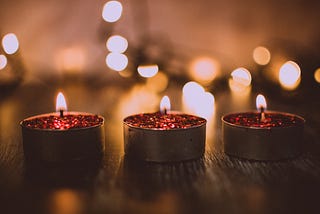 Shows three pink tealight candles burning in the dark with blurry lights behind them