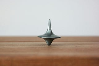 Silver metal top spinning vertical on a wooden table with a white background.