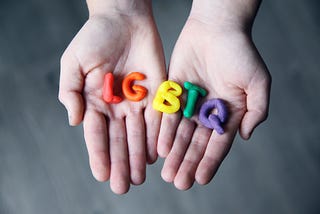 A person holding the letters “LGBTQ” made in colorful playdough.