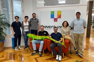 A photo of a seven-member data team with an iguana across the front two people’s laps.
