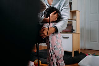 Woman seated at a desk with a computer on it comforting a toddler in pink pajamas