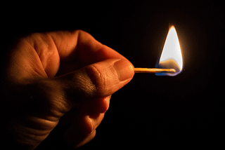 Image of a hand in the deep darkness, holding a flaming match.