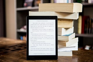 Ebook reader leaning against a stack of paperback books.